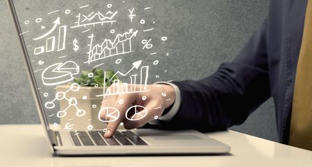 Sales person in suit using a laptop to calculate pie chart and exponential growth statistics on office desk concept