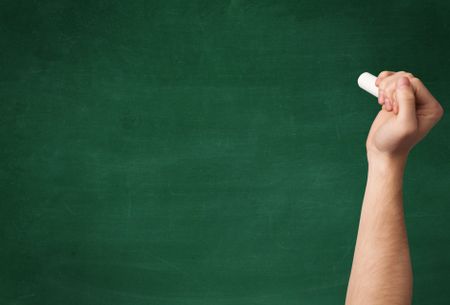 A mature hand writing or drawing on a clean green blackboard with a white chalk.