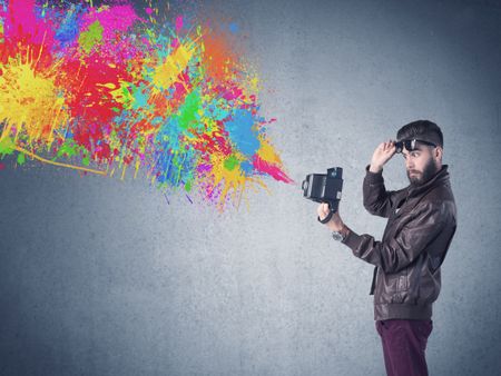 A retro hipster male taking photograph with a vintage camera of an urban wall with paint splatter concept