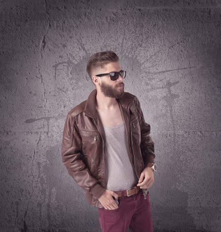 A hipster fashion model guy in casual clothing stnading with mobile phone in front of concrete urban wall background concept