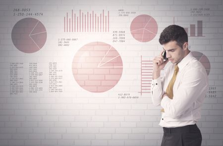 Young sales business male in elegant suit standing in front of brick wall background with lines and pie charts concept