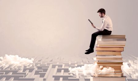 A businessman with laptop tablet in elegant suit sitting on a stack of books on top of sandy labirynth background concept