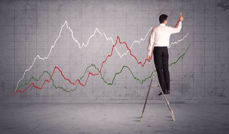 A guy in modern suit standing on a small ladder and drawing a chart on grey wall background with exponential progressing curves, lines