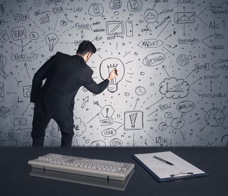 An intelligent office worker drawing strategy ideas and future plan keywords on wall at a brainstorming meeting in office concept