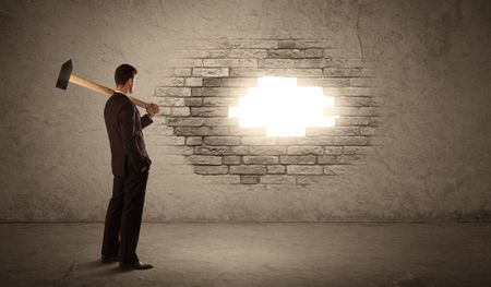 Business man hitting brick grungy wall with hammer and opening a hole