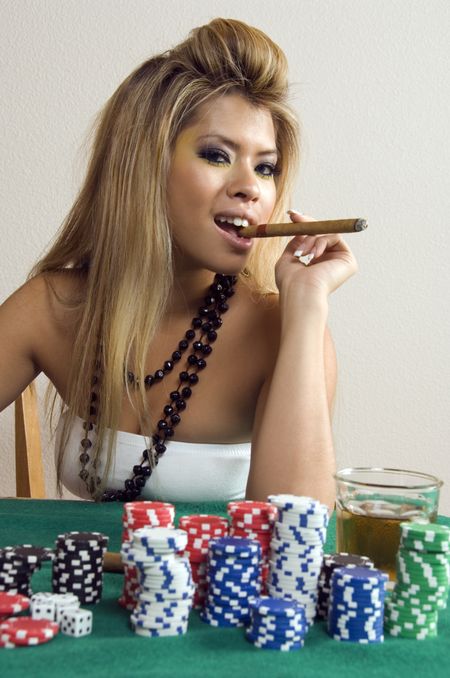 Sassy young Asian-American woman holds cigar between her teeth near stacks of poker chips and drink