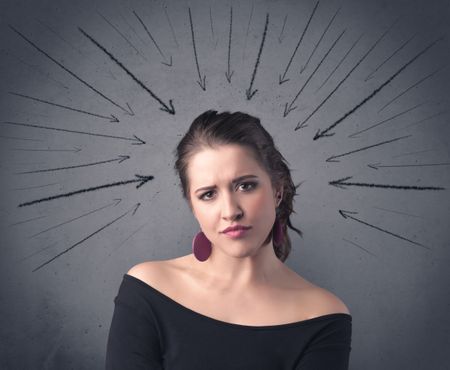 A teenage student girl under pressure while making happy face expressions illustrated with black arrows pointing at her head on the wall blackground concept.