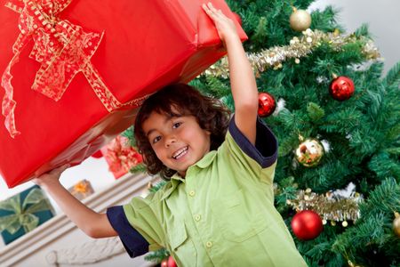 Boy next to the tree lifting a Christmas present
