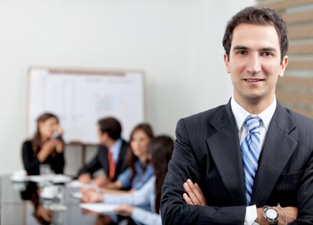 Friendly business man portrait smiling in his office with his team behind him