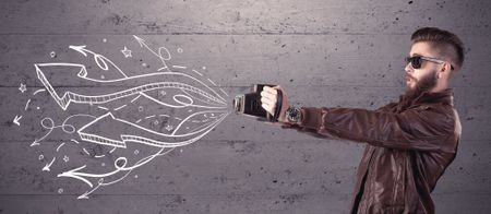 A hipster guy opening his point of view through looking a vintage camera concept with illustratied drawn arrows on urban wall