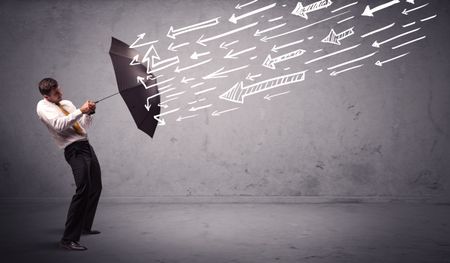 Business man standing with umbrella and drawn arrows hitting him on grungy background