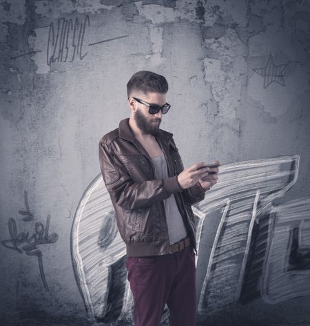 A handsome hipster guy with beard and sunglasses standing in front of an urban wall with graffiti concept