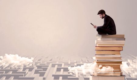 A businessman with laptop tablet in elegant suit sitting on a stack of books on top of sandy labirynth background concept
