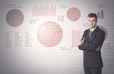 Young sales business male in elegant suit standing in front of brick wall background with lines and pie charts concept