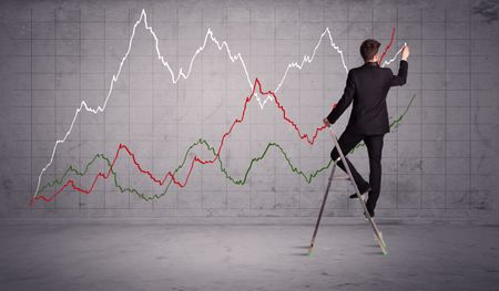 A guy in modern suit standing on a small ladder and drawing a chart on grey wall background with exponential progressing curves, lines