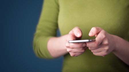 Young woman holding smarthphone in hand while typing