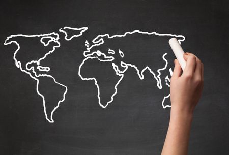 A teacher drawing the map of the world on a blackboard with a chalk