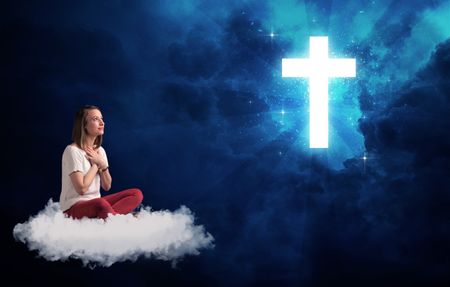 Caucasian woman sitting on a white fluffy cloud looking at a big, bright; blue; glowing cross