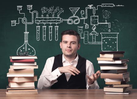 A young chemistry teacher in the middle of a chemical process explanation with tubes, reactions drawn on the blackboard back to school concept.