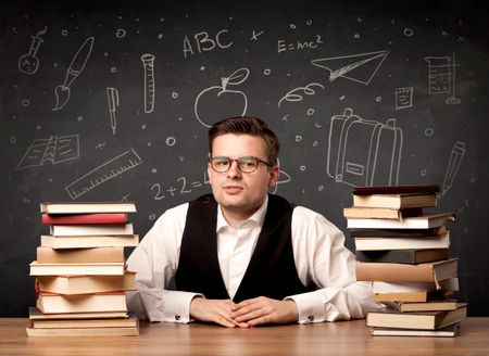 A passionate young teacher sitting at school desk with pile of books in front of blackboard drawn full of back to school items concept.