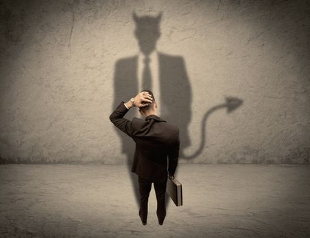 An experienced tricky businessman in suit looking at his devil desguise shadow reflected on the wall concept