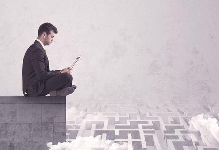 Business worker sitting on concrete building edge, thinking of solving a maze concept with labyrinth and clouds