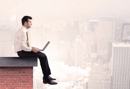 An elegant businessman in modern suit sitting on the top of a brick building, looking over the cityscape with clouds concept