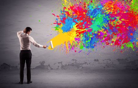 An elegant businessman in suit painting colorful splatter, bright colors on grey urban wall with a paint roller in his hand concept