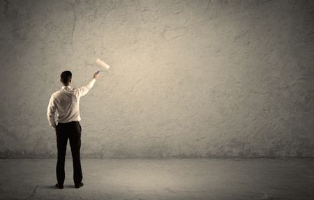 An elegant businessman in suit holding a paint roller, standing with his back, facing an empty urban concrete wall concept