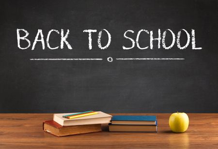 Back to school concept with writing on blackboard in capital letters and a desk with papers, fruit