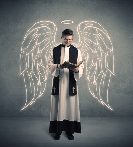 A young male priest with drawn large angel wings standing with the holy bible in his hands concept.