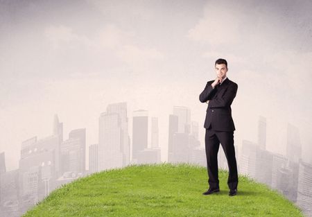 A confident male well looking office manager standing in small green grass in front of city landscape with tall buildings concept.