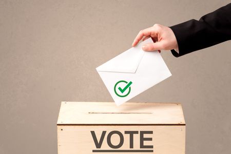 Close up of male hand putting vote into a ballot box, on grunge background