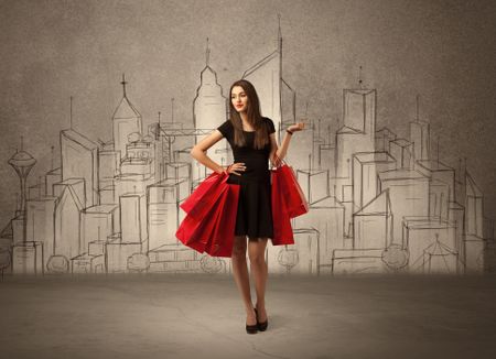 An attractive young lady standing with red shopping bags in front of drawn city landscape silhouette concept