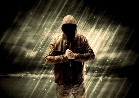 An incognito hooded stalker standing in the rain with his back in front of dark scary landscape concept