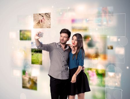 Collecting memories concept with photos in backbround and a happy young couple in love taking selfie with a mobile phone