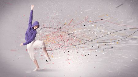 A young contemporary energetic dancer in action in front of a grey wall background with lines, spray dots and splatter concept