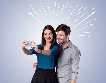 A cheerful young couple taking selfie photo with mobile phone and white lines and arrows pointing to the sky above them concept