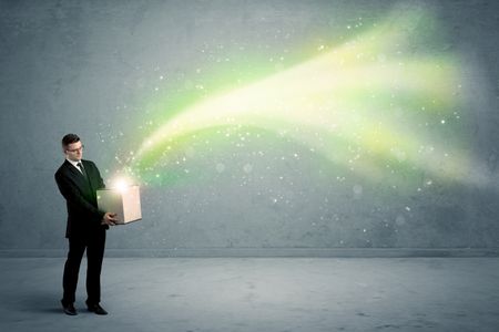 Bright yellow, green light beams escaping a cardboard box held by young elegant male business person in stylish suit concept.