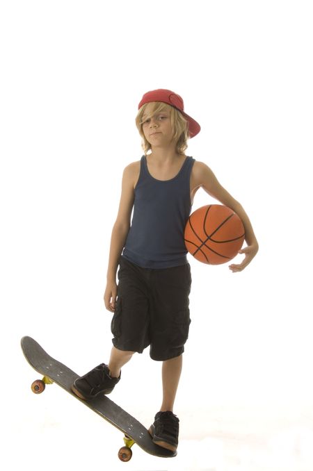 Caucasian boy of ten with long blond hair holds basketball and stands balanced on end of skateboard