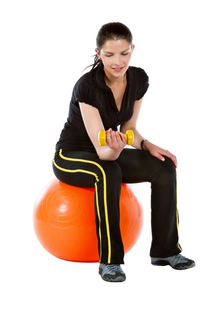 Beautiful woman exercising with free weights sitting over an orange pilates ball