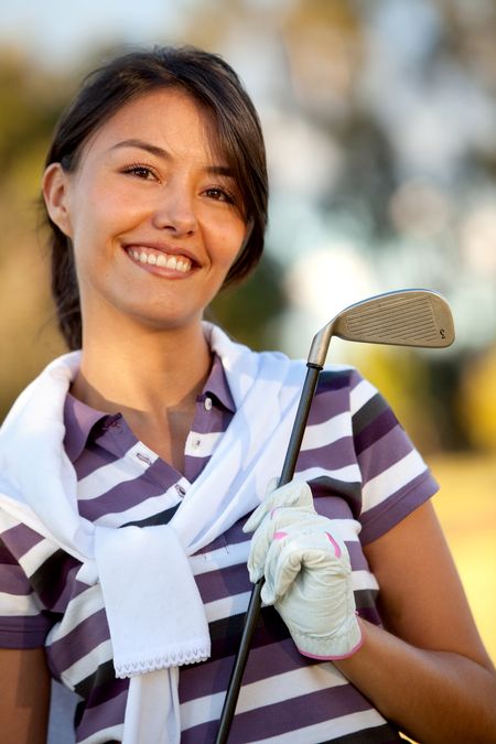 Female golf player outdoors holding a club and smiling
