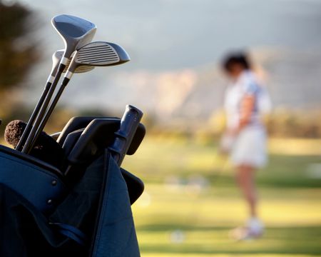 Bag of golf clubs outdoors - female player on the background