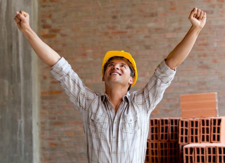 Happy construction worker at a building site with arms up