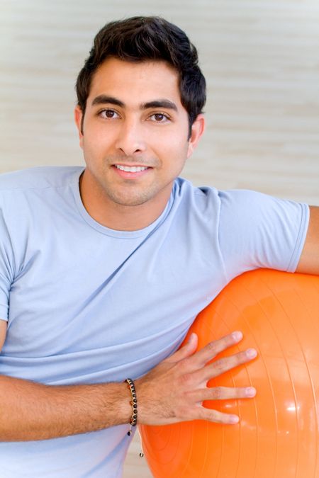 handsome man portrait at the gym smiling leaning on a pilates ball
