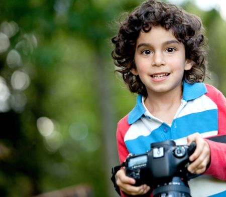 Beautiful boy holding a camera outdoors and smiling