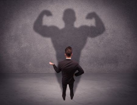 A young salesman standing with his back, looking at his musculous shadow reflecting on the wall concept