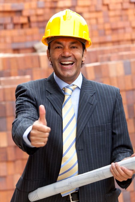 Happy engineer holding a model in a construction with his thumb up