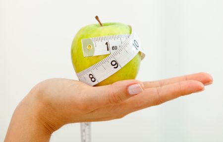 Hand holding an apple with a measuring tape around it isolated over a white background