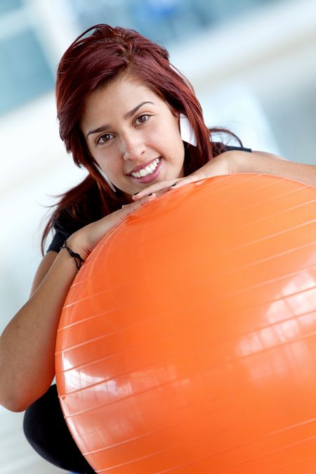 fitness woman smiling and leaning on a pilates ball at the gym